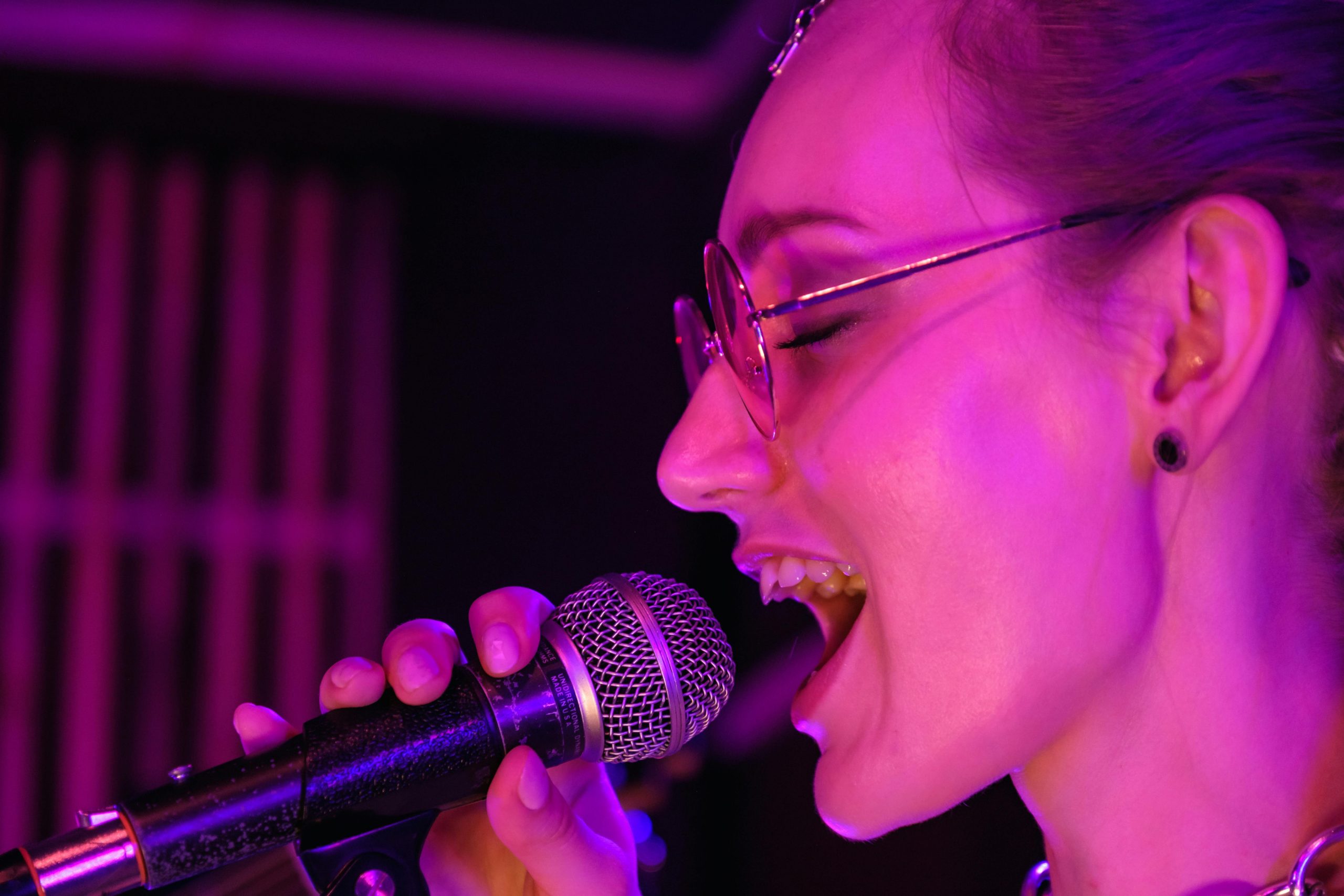 A vibrant close-up of a female singer performing with passion under purple stage lights.